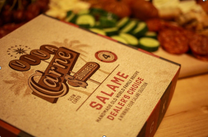 A Viva Carne Salame Gift Box by a cheese board